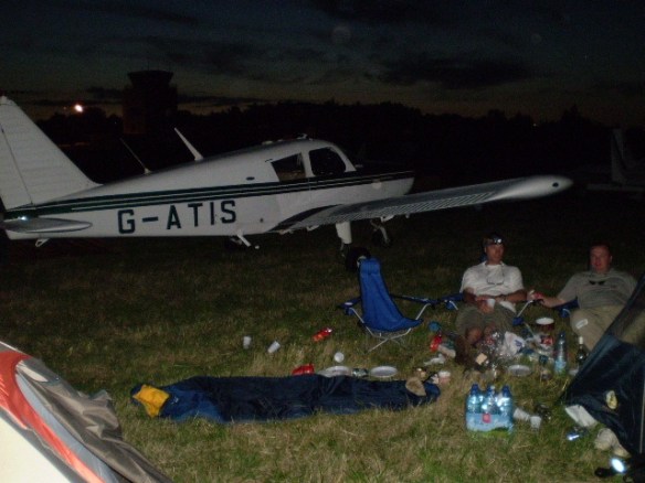 Cherokee G-ATIS parked in front of a a group of people sitting in camp chairs.
