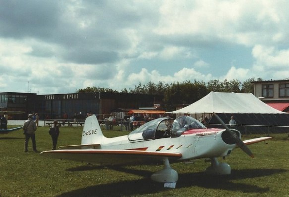 An Emeraude aircraft parked on grass, canopy open with a marquee in the background.