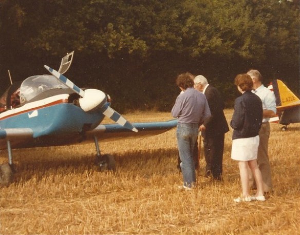A group of four people standing talking in front of a small aircraft.