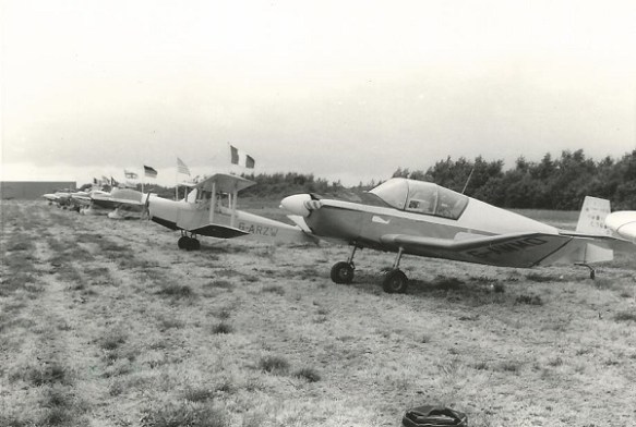 A monocrome picture of a row of light aircraft parked on a dry crass field.