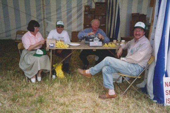A group of four people siting around a trestle table engaged in making medals.