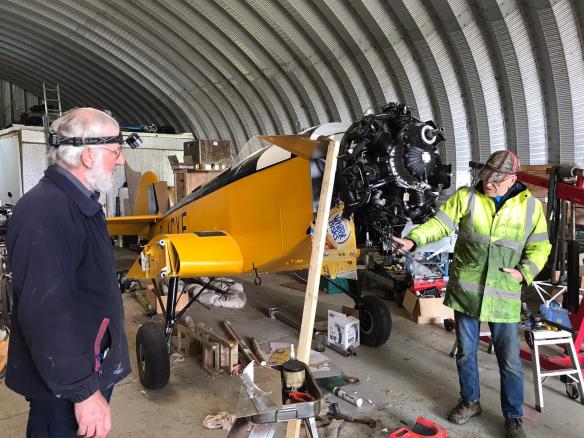 Two men standing near to a Klem aircraft in a hanagar, in discussion.