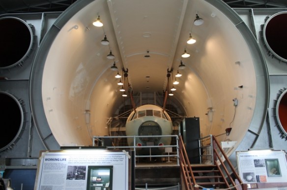 A view down an enormous clyndrical chamber containing the nose of a commercial aircraft.